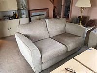 Front view of light beige loveseat sofa in textured fabric, showing two seat cushions and two back cushions, wide padded arms, placed in living room setting