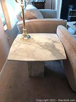Top-down view of square polished marble side table with natural veining, placed between sofas with a brass lamp on top.