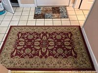 Photo showing a red Persian inspired area rug measuring 3x5 feet in front of a doorway with a smaller door mat in the background.