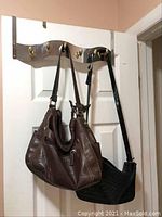 Two leather handbags hanging on hooks on a door; one brown, one black.