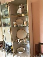 Glass cabinet with displayed items including ceramic figurines, Lenox cake plate, glass and crystal vases.