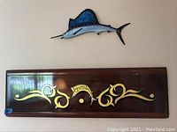 Wall mounted display of wooden panel with gold design and a metal swordfish sculpture above it