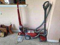 Full view of two Electrolux vacuums side by side on carpet against wall showing upright and canister models with accessories.