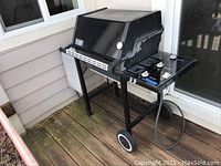 Black Weber gas grill with side burner on deck patio, showing overall condition and frame