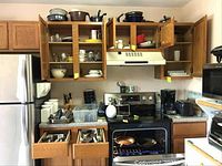 Full kitchen setup showing refrigerator, stove, cabinets with open doors, drawers open revealing flatware and kitchen tools.