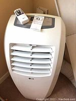 Front view of white LG portable air conditioner with vent and digital display on top and remote control placed on it.