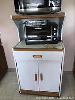 Front view of white kitchen cabinet with wooden handles and trim, showing a microwave and toaster oven on top (not included).