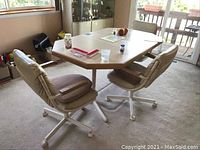 Full view of the dining table with three vinyl covered chairs showing shape, color, and condition.