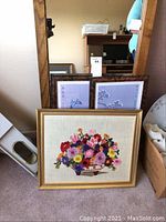 Photo of large mirror with chestnut wood frame, two smaller framed Asian-themed pictures behind it, and crewel embroidery framed floral piece in front.