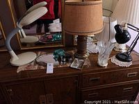 Photo showing entire lot on wooden dresser including all lamps, mirror tray with broken glass, opera glasses, and part of mirror in background.