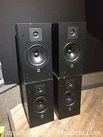 Four black KEF Model P60 speakers stacked on floor.