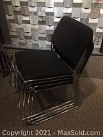 Four black fabric stacking chairs with straight looped chrome legs stacked together showing the condition and design.