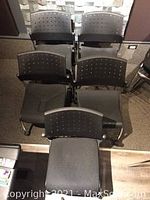 Five black stacking chairs arranged in two rows showing the perforated plastic backs and fabric seats.