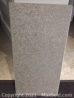 Close-up photo of a single rectangular luxury vinyl flooring tile with a grey concrete texture and pattern.
