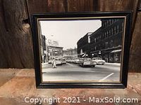 Framed black and white photograph showing a 1950s street scene with cars and buildings in a vintage city environment.