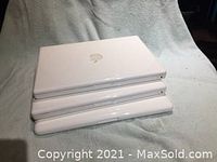 Three stacked closed white MacBook laptops showing top covers