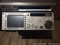 Front panel view showing LCD monitor, transport controls, jog/shuttle wheel, and cassette slot above.