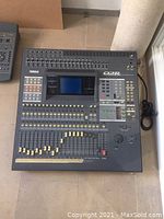 Top-down view of Yamaha 02R console showing faders, LCD screen, buttons and attached power cable