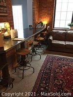 Four wooden seats with curved backs on steel bases arranged under a bar counter in a studio setting.