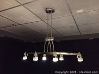 Fixture mounted on a ceiling and lit up, showing six conical light heads arranged on a triangular metal frame.