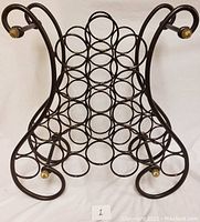 Front view of metal wine rack showing circular holders and scroll frame ends with brass/gold knobs.