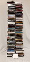Full vertical view of over 100 CDs stacked in two columns on a CD rack, showcasing height and quantity.