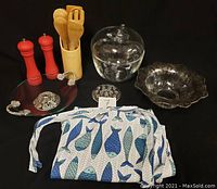 Kitchen accessories including red salt and pepper shakers, wooden spoon set in holder, glass punch bowl with apple lid, footed glass bowl with floral pattern, round decorative glass tray with metal handles, flower frog, silver decorative plate, and fish patterned towel.