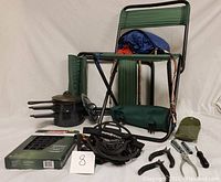 Full lot layout showing two foldable green camping chairs, three black camp pots with lids, Coleman waffle iron in box, easy pack coat in fanny pack, Snowtrax shoe grips, and assorted hand tools including pliers and screwdriver.