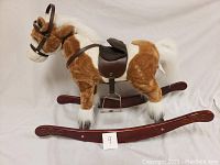 Full side view of the child's plush rocking horse showing brown and white plush fur, black saddle, and wooden rockers with decorative ends.