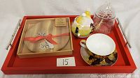 Full lot on red tray showing all included items - teapot, mug, saucer, honey pot, wood board, serving tool