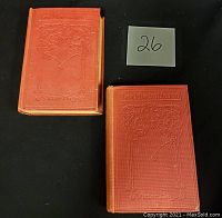 Two red cloth hardcover books titled Les Miserables by Victor Hugo, embossed cover design, placed side by side on a black surface with lot number.