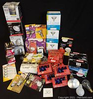 Wide view of all lightbulbs and assorted lighting items included in the lot, showing original packaging, various brands and bulb types.