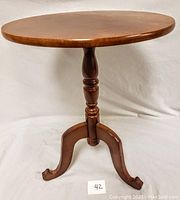 Full side view showing the round table with central turned pedestal and three curved legs in medium brown wood finish.