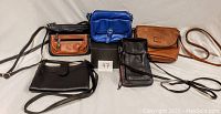 Five leather handbags displayed together showing various colors: black, brown, blue, with shoulder straps.