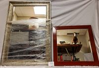 Both mirrors wrapped with protective plastic, a large rectangular silver-framed mirror and a smaller square reddish-brown framed mirror shown together.