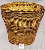 Front view of large wicker basket showing woven lid and body, with handles on sides.