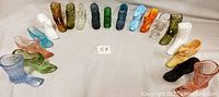 Nineteen glass shoe figurines displayed in a semicircle, showing variety in color and style.
