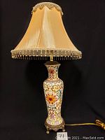 Full view of the oriental style lamp showing base with colorful floral scroll decoration and fabric lampshade with beaded trim.