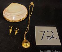 Photo of seashell jewelry box, gold-toned necklace with spiral pendant, pair of gold-toned shell-shaped earrings on black background with lot number card.