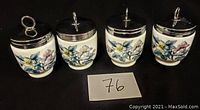 Front view of four Royal Worcester egg coddlers showing floral patterns and metal lids with loop handles.