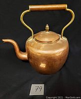 Front view of vintage copper teapot showing rounded body, brass handle with wooden grip, and curved spout.