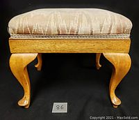 Front view of the wooden foot stool showing the cushioned upholstered seat, wooden frame, and cabriole legs.