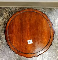 Top view of the round table showing scalloped edge trim, wood grain surface, and measurement tag.