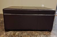 Front view of the dark brown leather storage bench with visible stitching and short wooden feet.