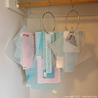 Stencils hanging on metal rings showing various decorative patterns including borders, floral, and geometric designs in translucent plastic sheets in colors like blue and pink.