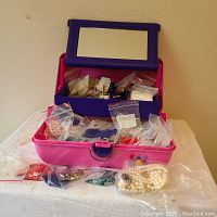 Photo showing pink and purple plastic jewelry organizer tote open with bags of beads inside.