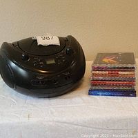 Front and side view of Memorex black portable CD player with stacked six CD cases beside it.