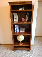 Front view of wood bookshelf containing globe, books, DVDs, VHS tapes, koala bookend, and dragon votive.