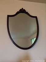 Full view of shield-shaped wood framed mirror hanging on the wall.
