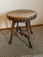 Full view of the round oak stool showing top and carved legs with brass claw feet on carpet.